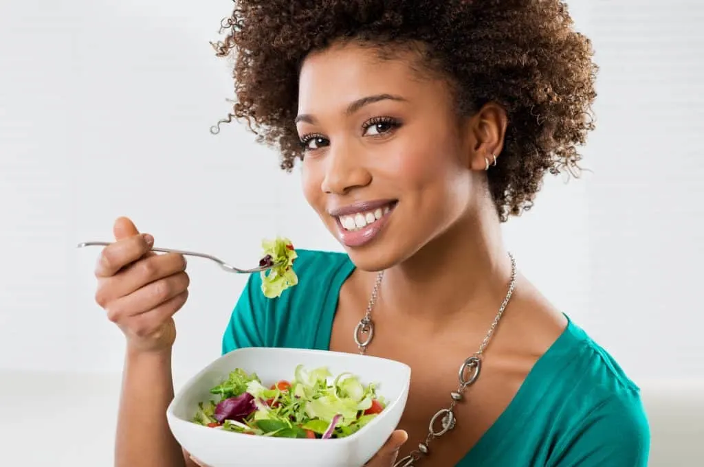 Woman wearing a green top Eating Salad At Home looking directly into the camera.