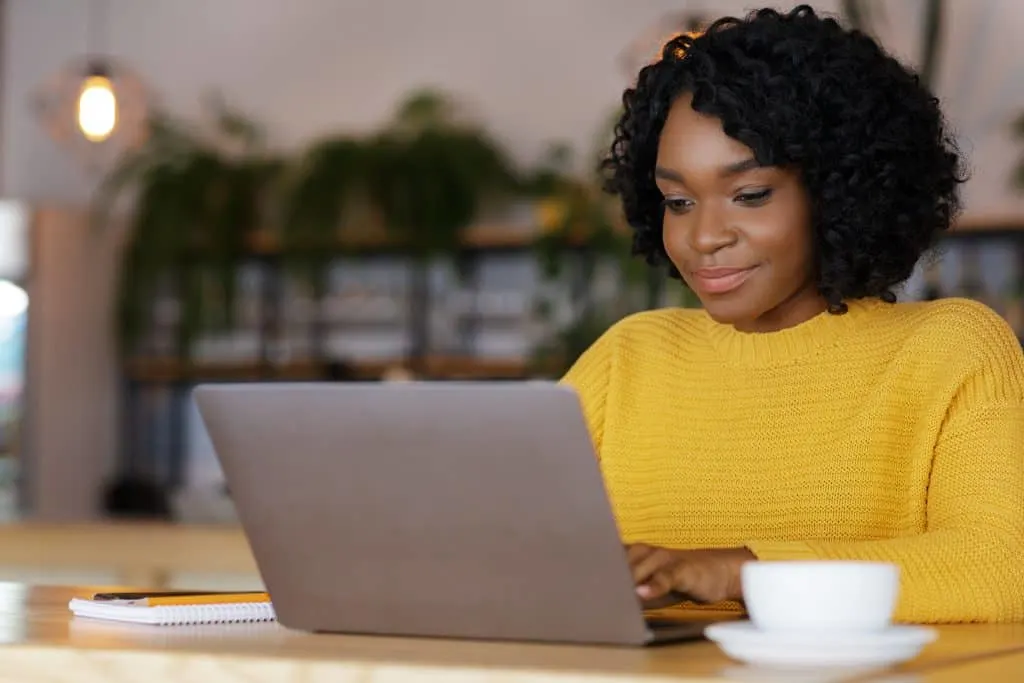 A female in a yellow sweater typing on her laptop searching the internet