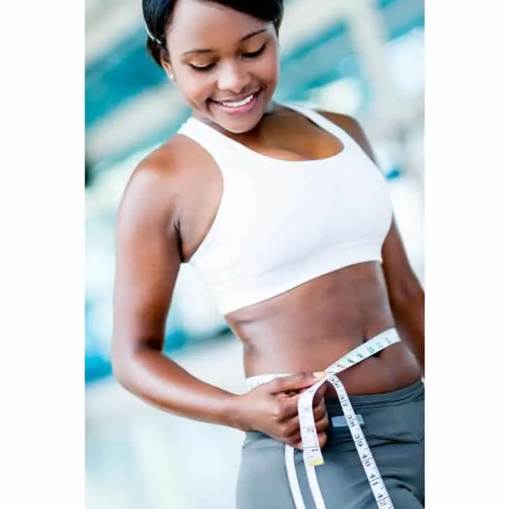 Woman wearing a white sport bra, measuring her waist on her weight loss journey
