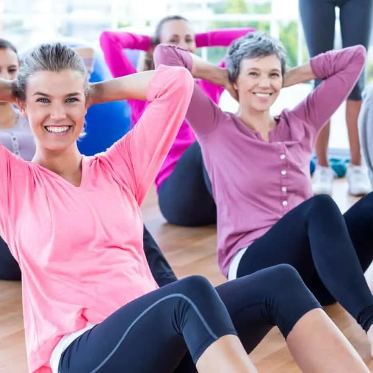 A group of cheerful women doing exercises on hard wood floor looking directly at camera